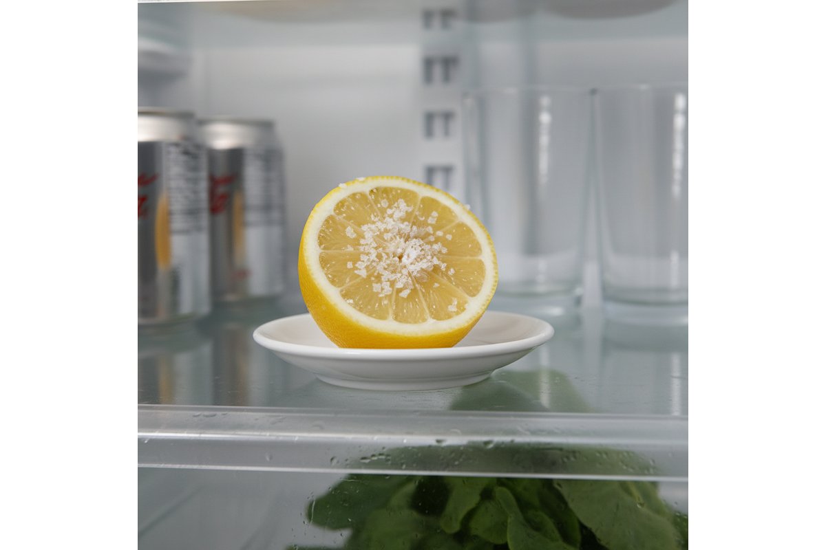 Mezzo limone su un ripiano del frigorifero accanto a vari alimenti.